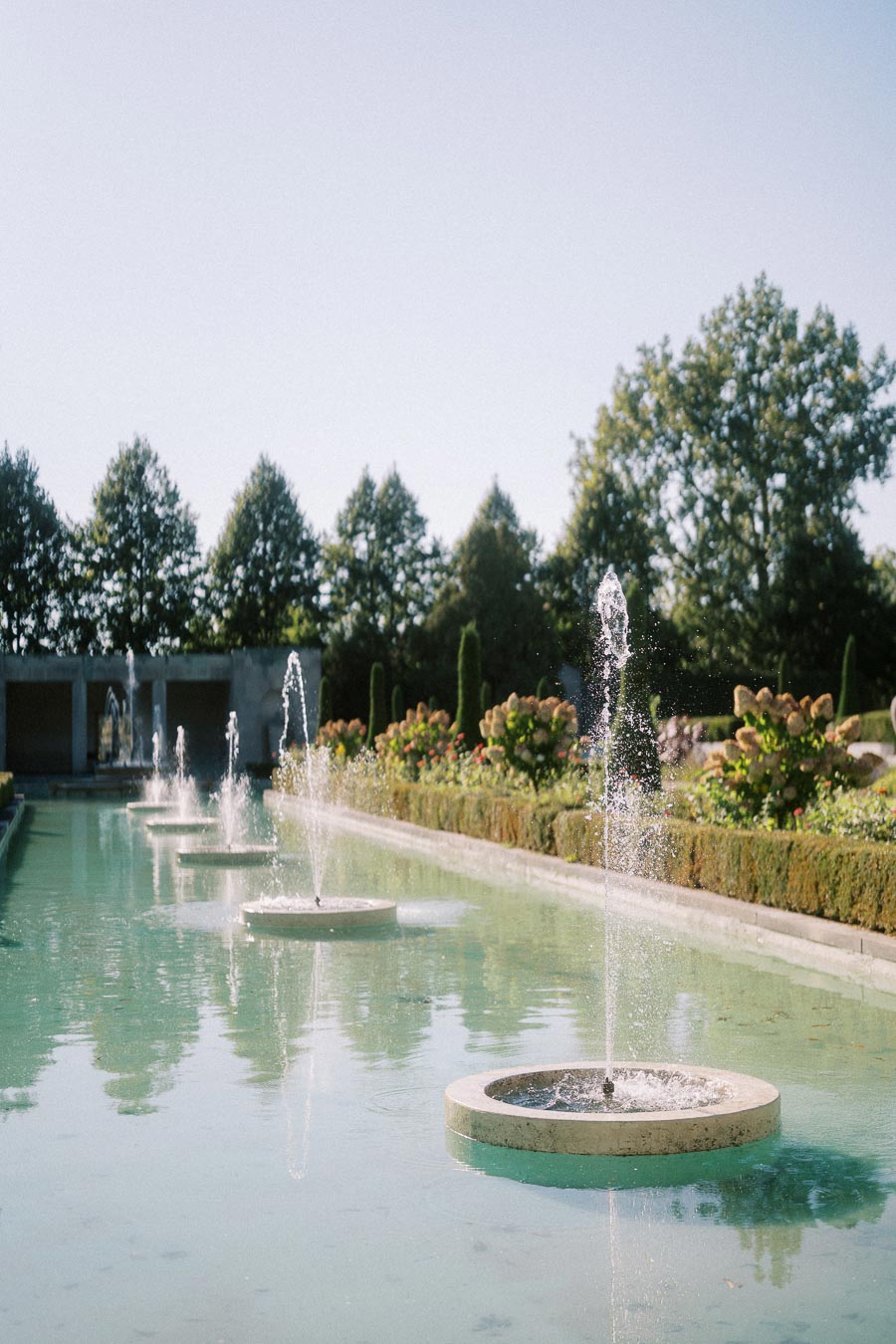 Tranquil garden fountains surrounded by lush greenery and vibrant flowers with a clear blue sky above