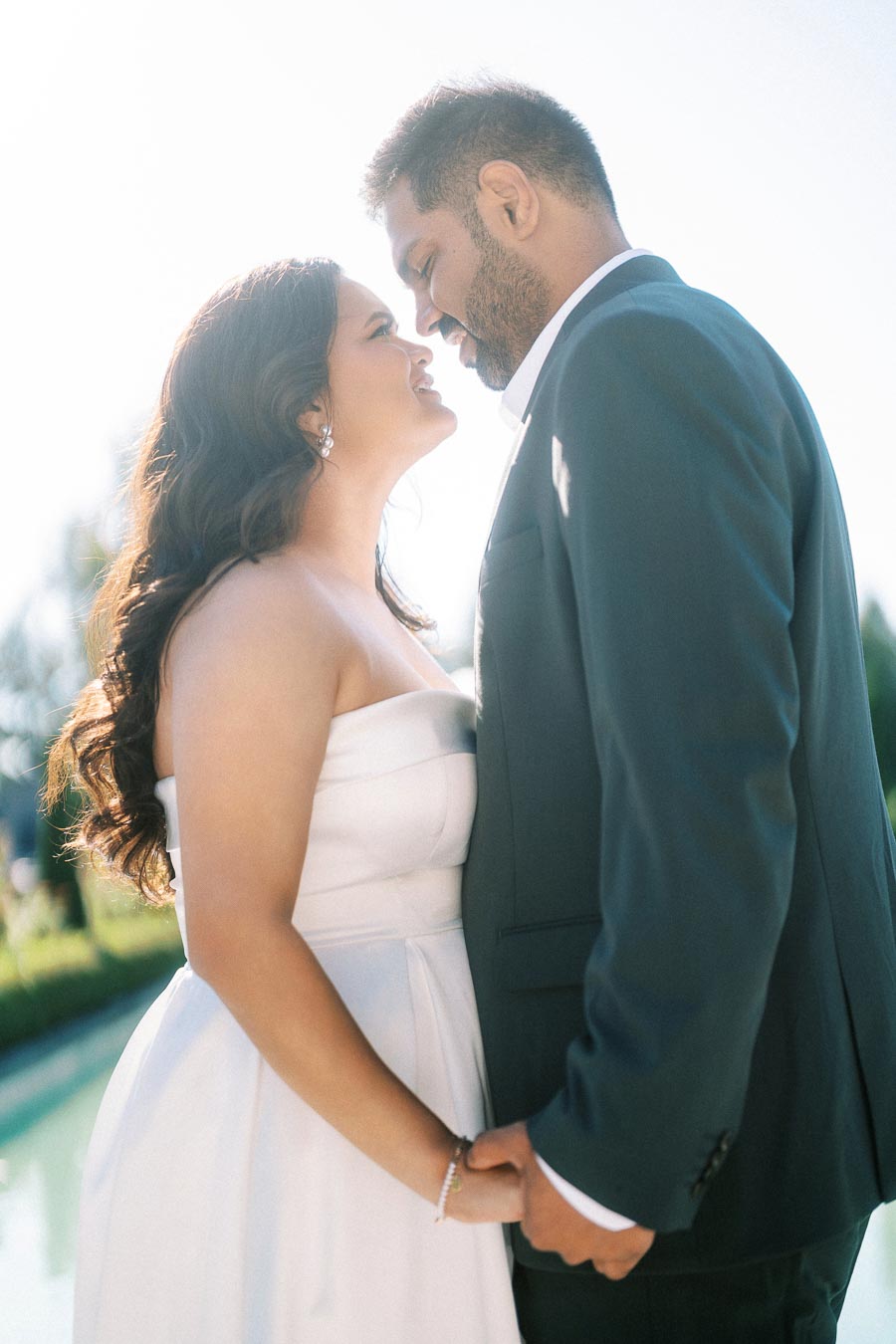 Romantic couple in wedding attire gazing lovingly at each other outdoors on a sunny day.