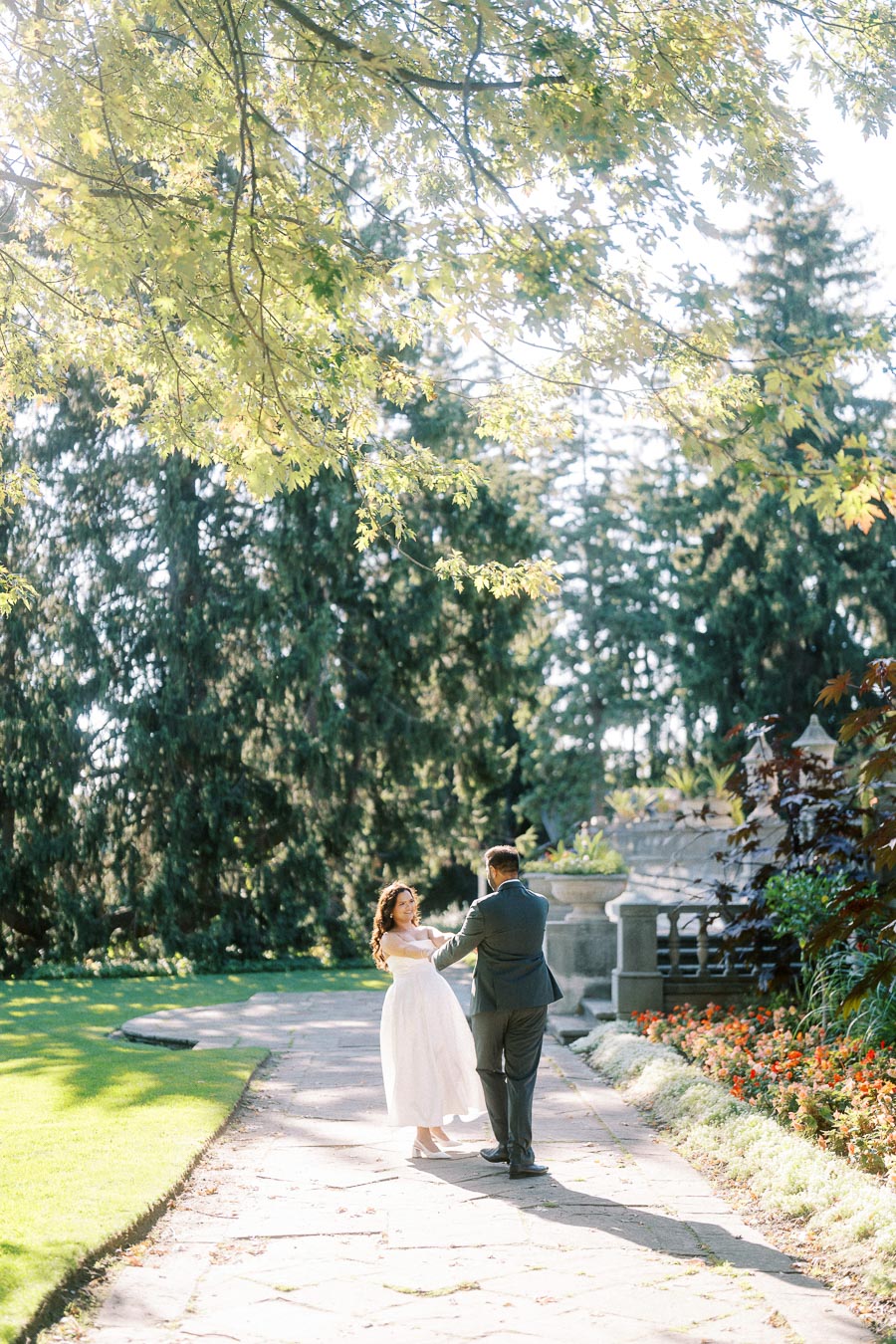 A couple dancing in a sunlit garden surrounded by lush greenery and vibrant flowers.