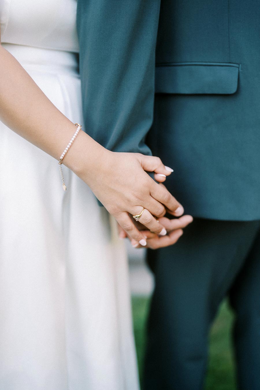 Close-up of a couple holding hands, with a focus on the woman's gold ring and pearl bracelet, showcasing a tender moment and love connection, suitable for wedding or relationship-related content.