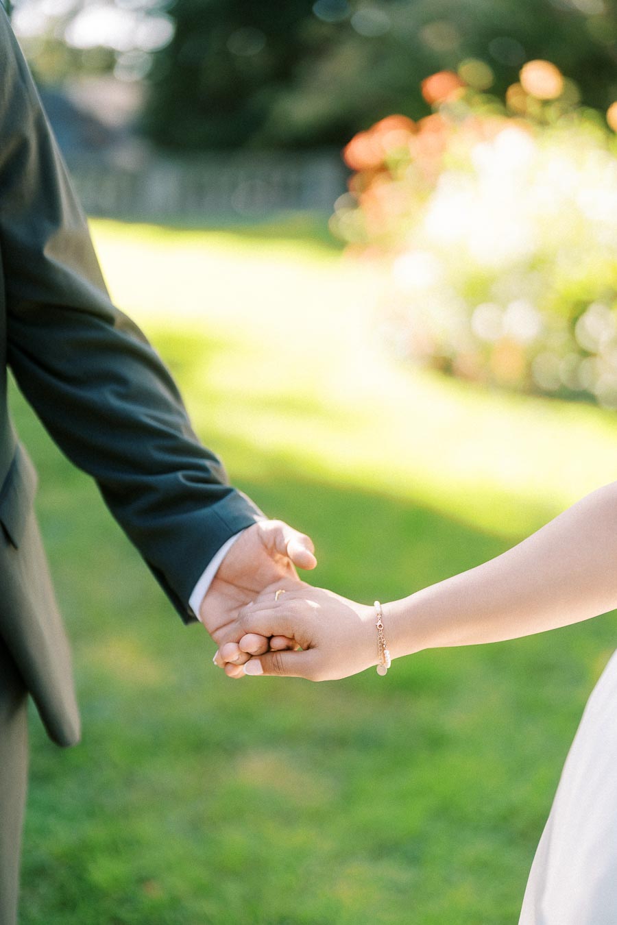 A couple holding hands in a garden, with a blurred green background and sunlight filtering through the trees, symbolizing love and togetherness.
