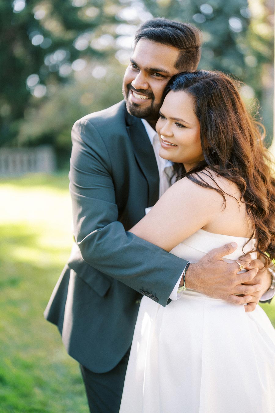 Happy couple embracing in a garden setting, dressed in formal attire, symbolizing love and togetherness.
