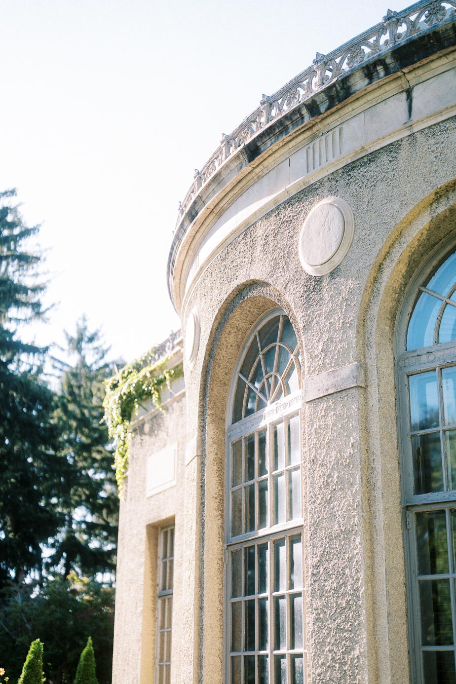 Elegant historic building with arched windows and detailed stonework, surrounded by lush greenery under a clear blue sky.