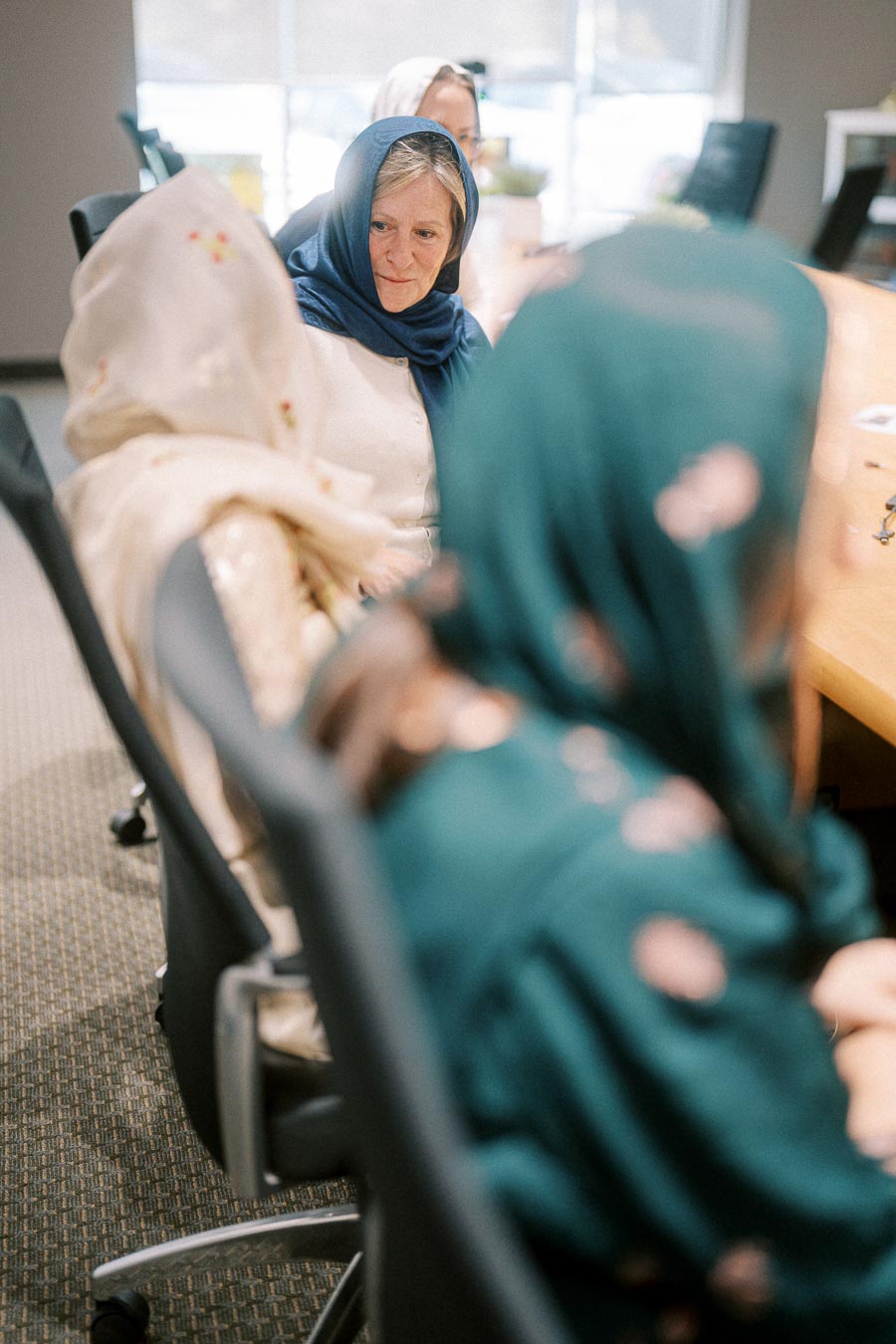 Women in headscarves engaged in conversation around a conference table, promoting cultural diversity and workplace inclusion.