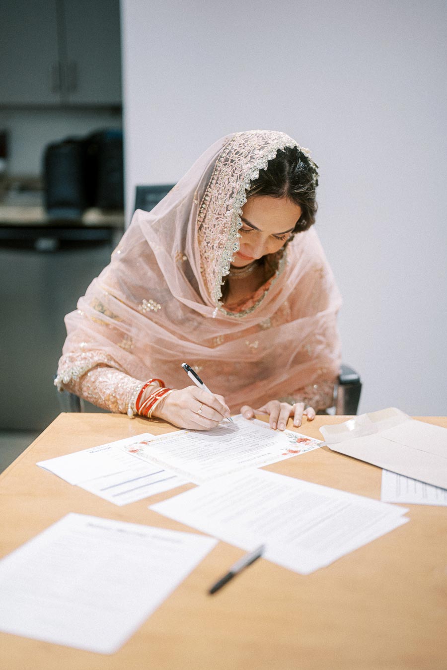 A woman in traditional attire signs documents at a desk, symbolizing an important agreement or contract.