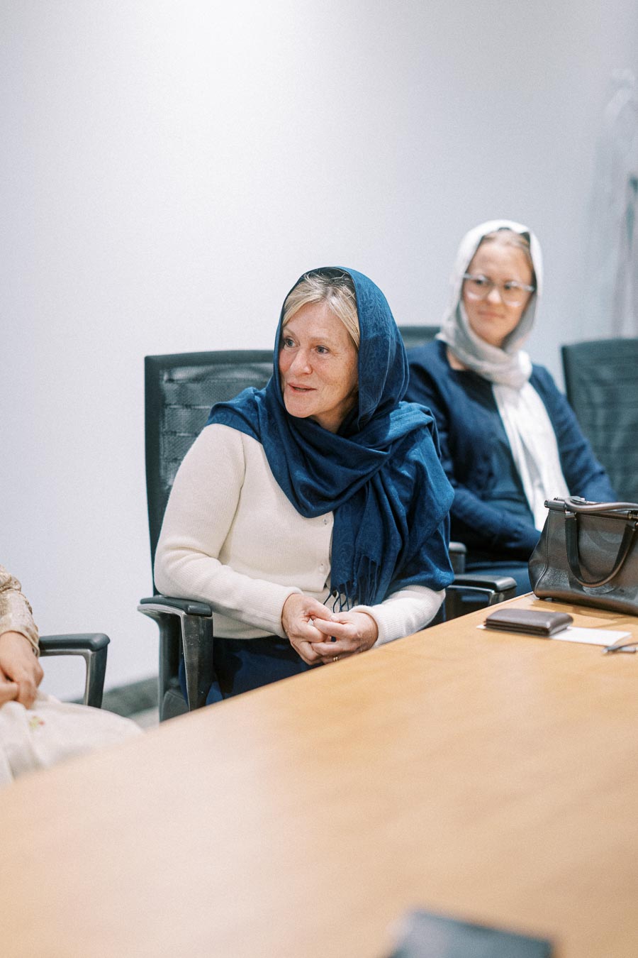 Two women in hijabs sitting at a conference table engaged in discussion during a business meeting.