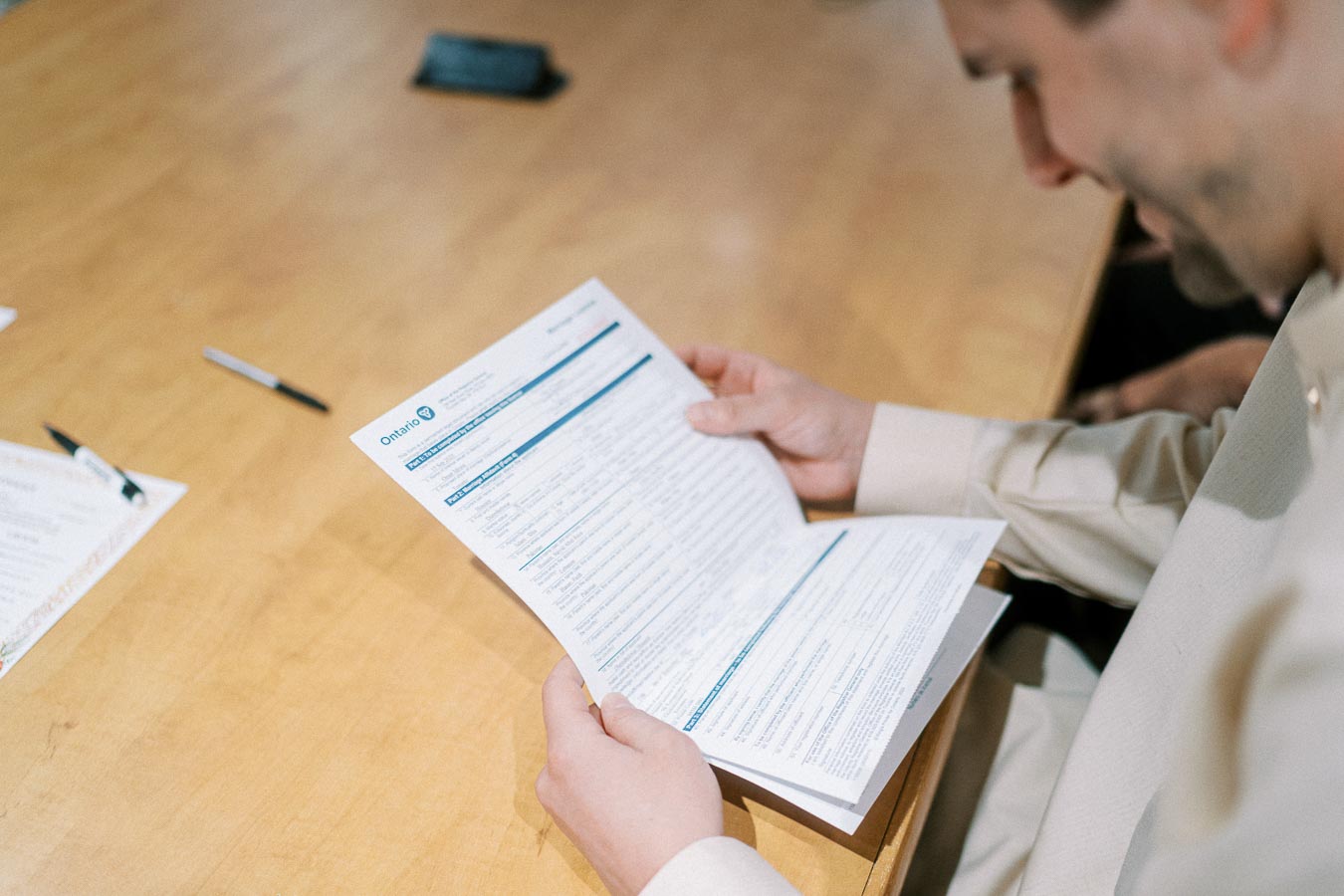A person reviewing an official document with Ontario letterhead at a wooden desk, with pens and papers visible nearby.