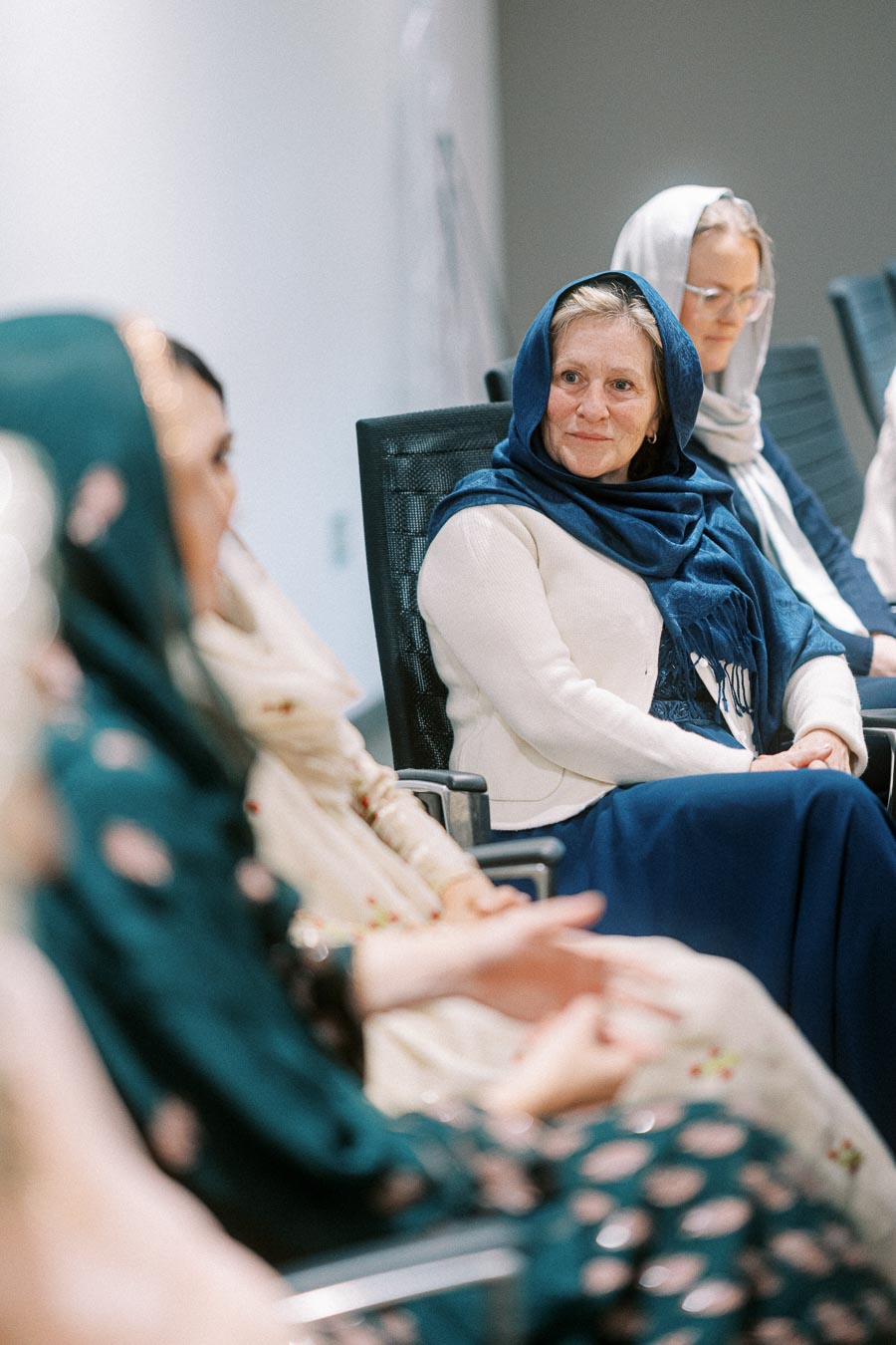 A diverse group of women wearing headscarves seated in a conference room, engaged in a thoughtful discussion.