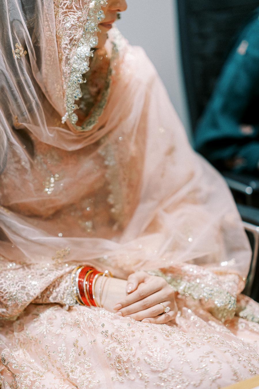 Close-up of a bride in an embellished pink lehenga, featuring intricate embroidery and delicate lacework, with hands adorned in red and silver bangles and a solitaire ring, perfect for South Asian wedding inspiration.