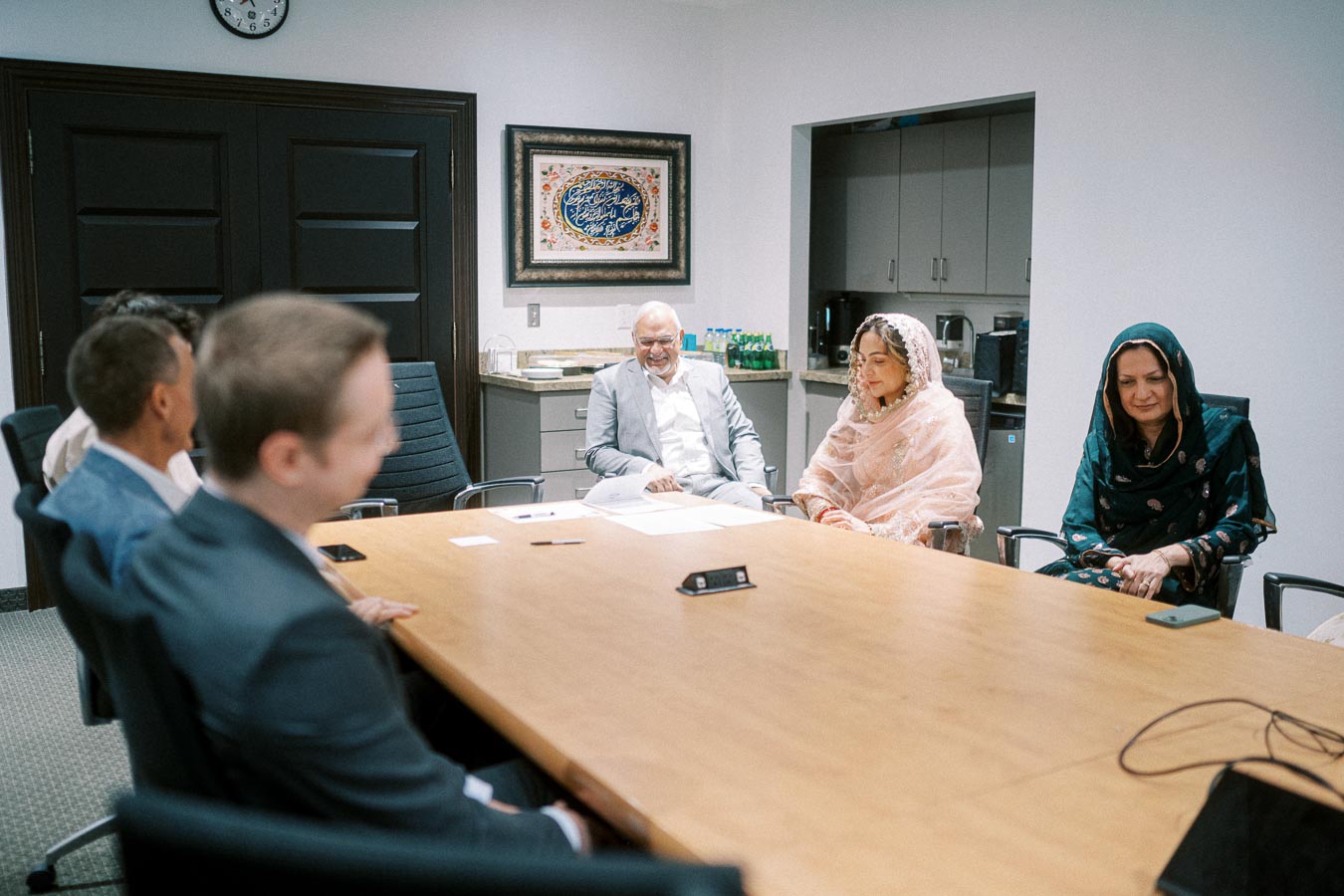 Group of professionals engaged in a business meeting in a conference room, featuring diverse clothing styles and traditional attire, emphasizing an inclusive work environment.