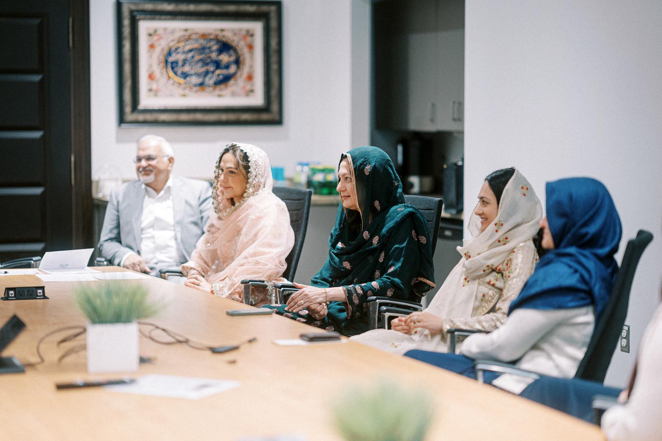 A diverse group of professionals in traditional attire engaged in a meeting, seated around a conference table in a modern office setting.