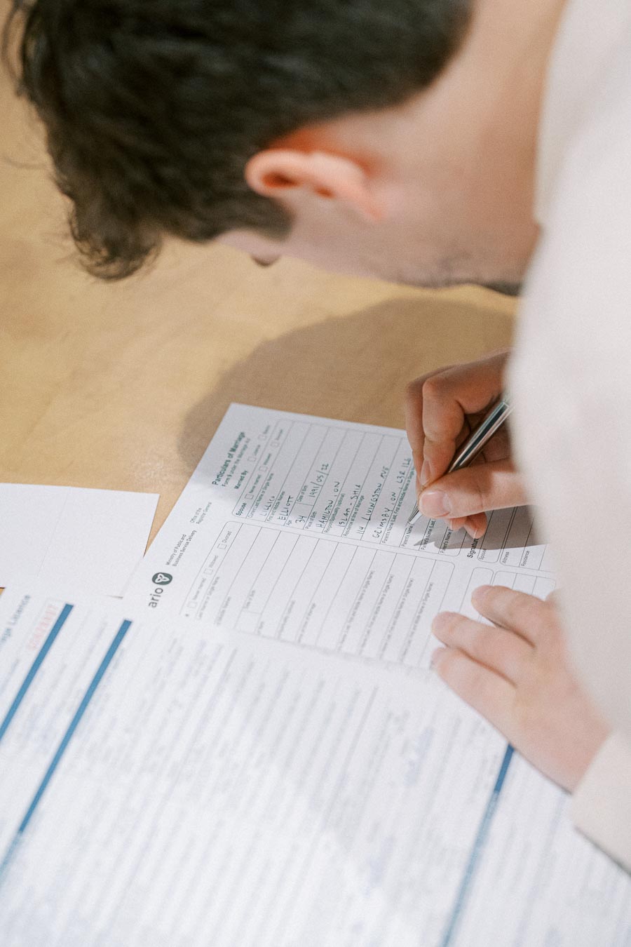 Person filling out paperwork with a pen on a wooden desk, focusing on document completion and details.
