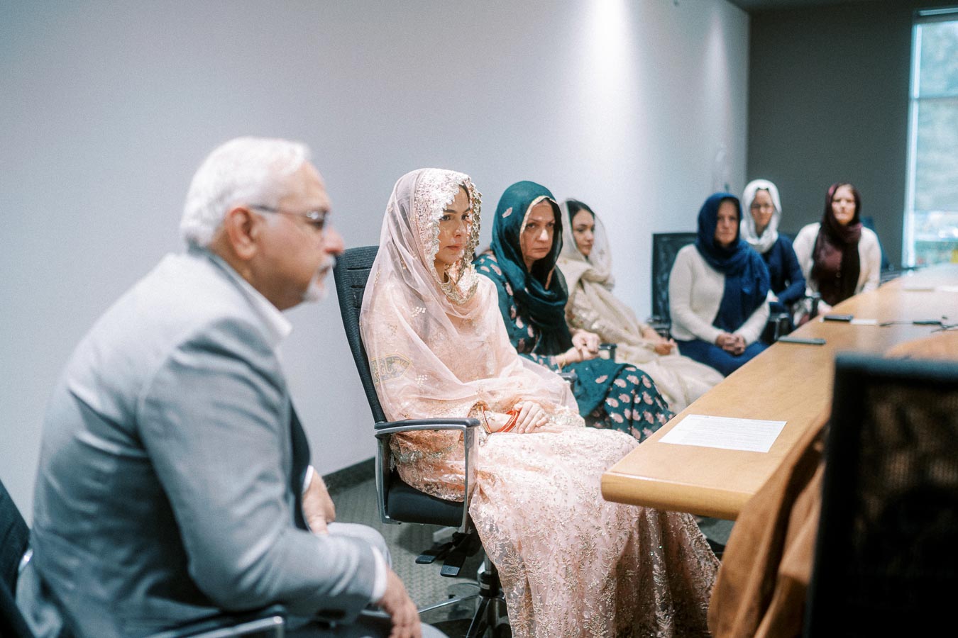 A diverse group of people in traditional attire sitting in a modern conference room, engaged in a discussion.