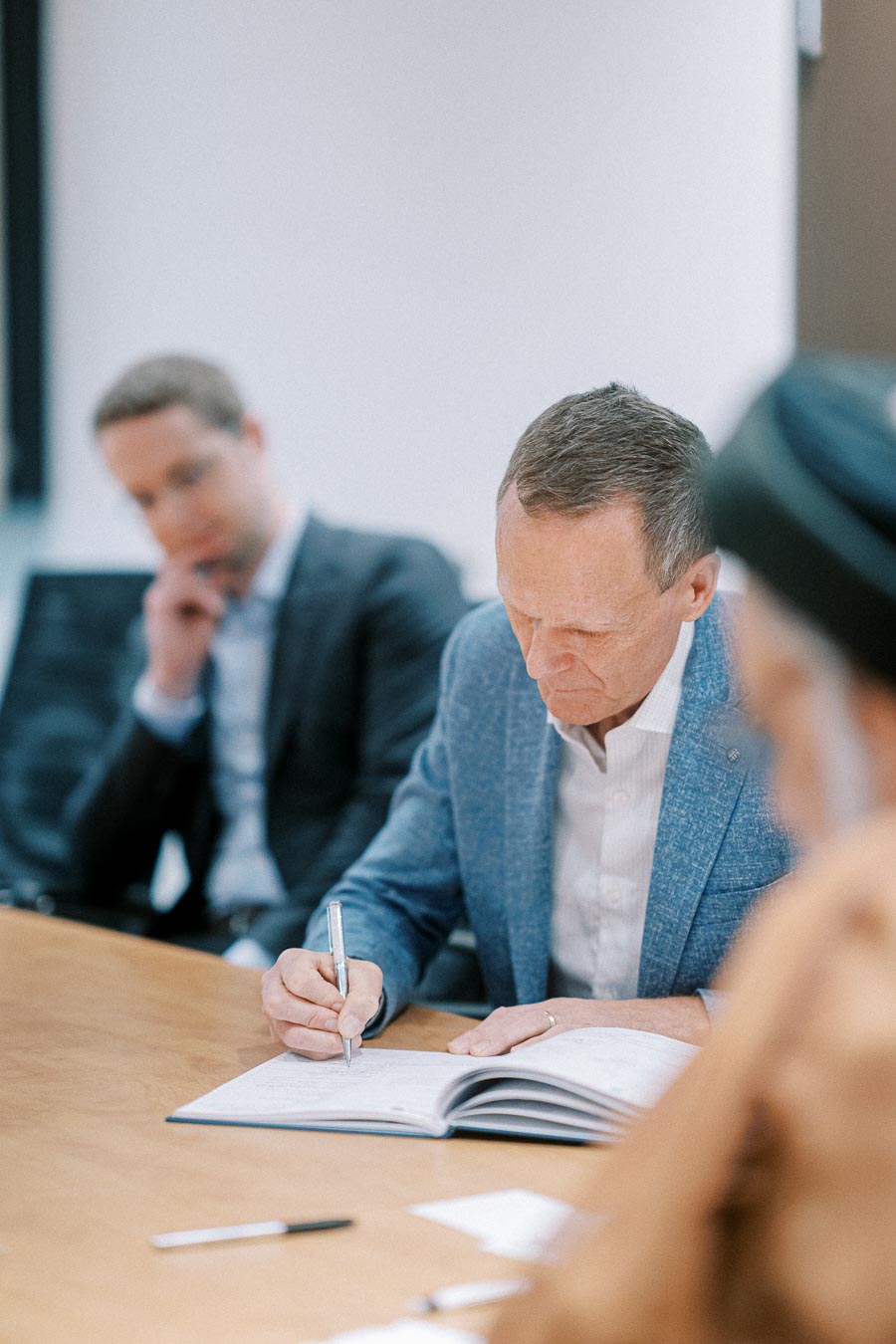 Business meeting with professionals in formal attire focused on writing in a notebook, illustrating teamwork and collaboration.