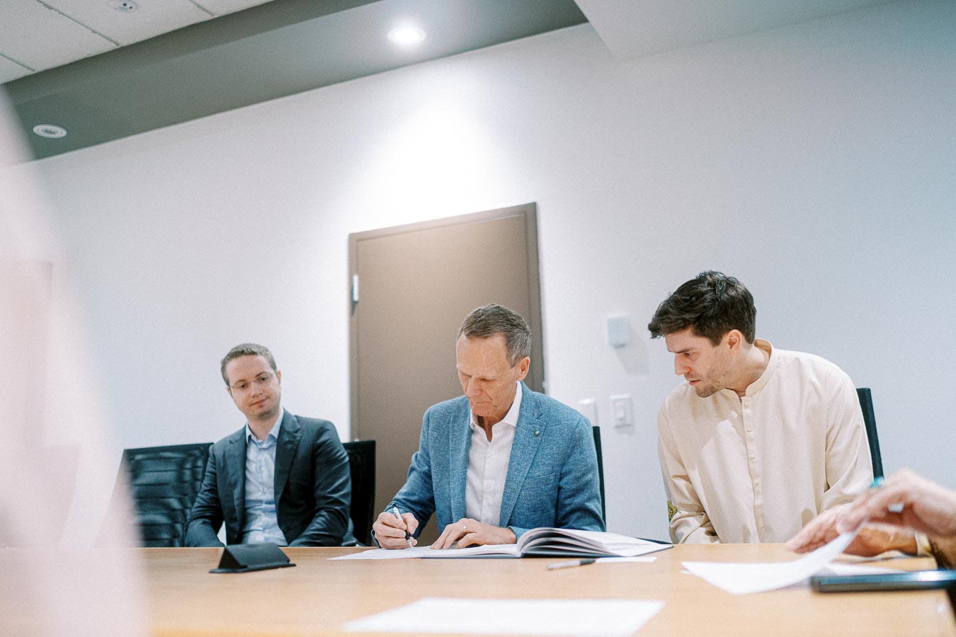 Business meeting with three men at a conference table reviewing documents in a well-lit office setting.