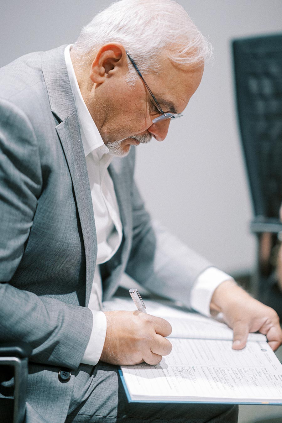 Mature man in a gray suit writing in a notebook during a business meeting.