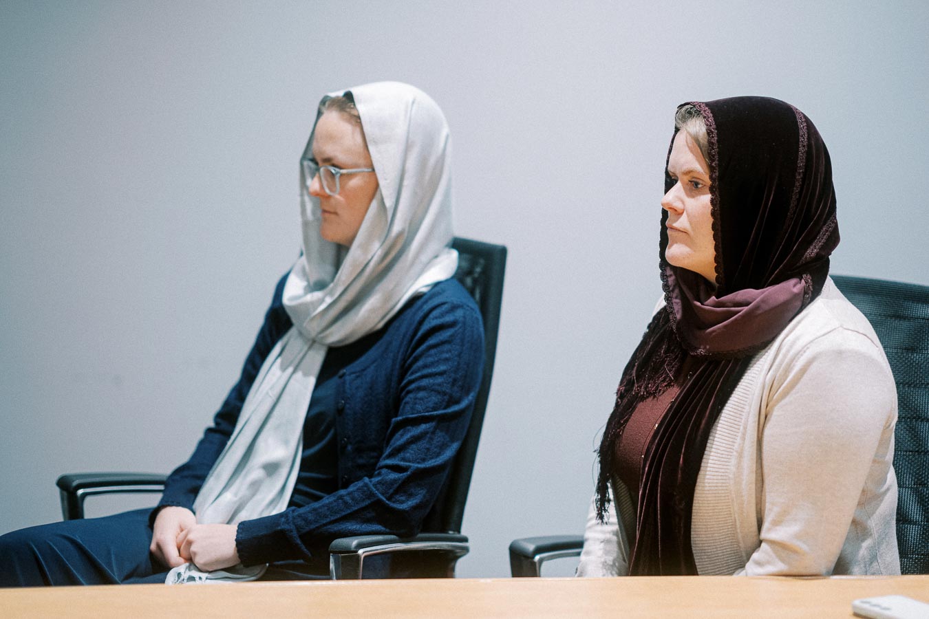 Two women wearing headscarves sitting attentively in a meeting room.