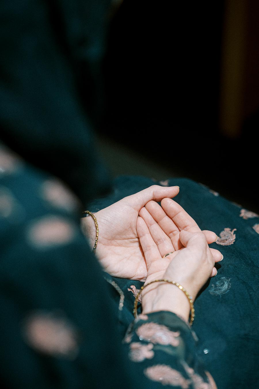Close-up of a person’s hands held together in a prayer position, wearing a dark, patterned garment.