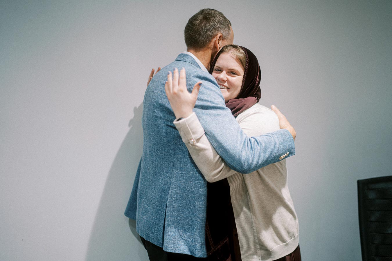 A person in a blue blazer and a person in a headscarf warmly embrace each other, showcasing a moment of joy and connection.