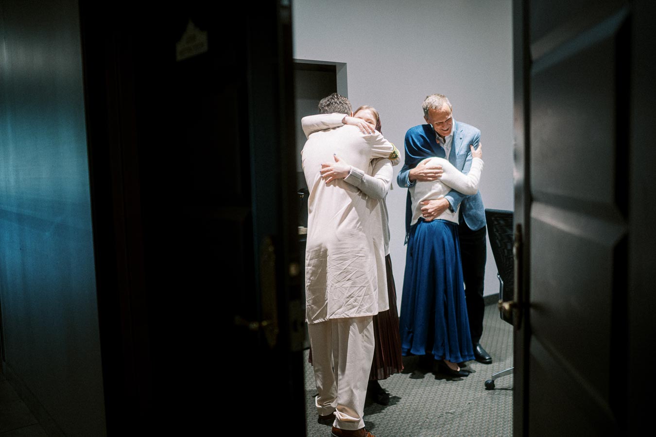 Group of four people embracing warmly in a room, sharing a moment of connection and friendship.