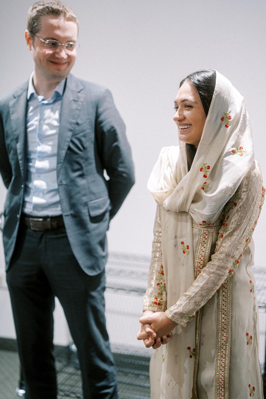 Two individuals smiling and interacting, with the woman wearing a traditional embroidered dress, suggesting a multicultural event or celebration.