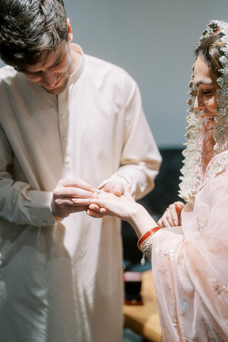 A groom placing a wedding ring on the bride's finger during a traditional wedding ceremony, with both wearing elegant attire.