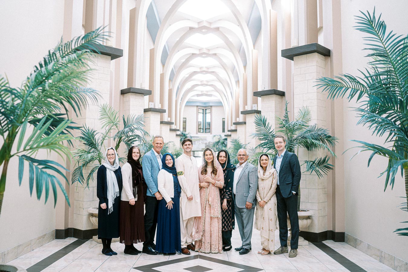 A diverse group of people posing in a modern architectural hallway adorned with greenery and arched ceilings.