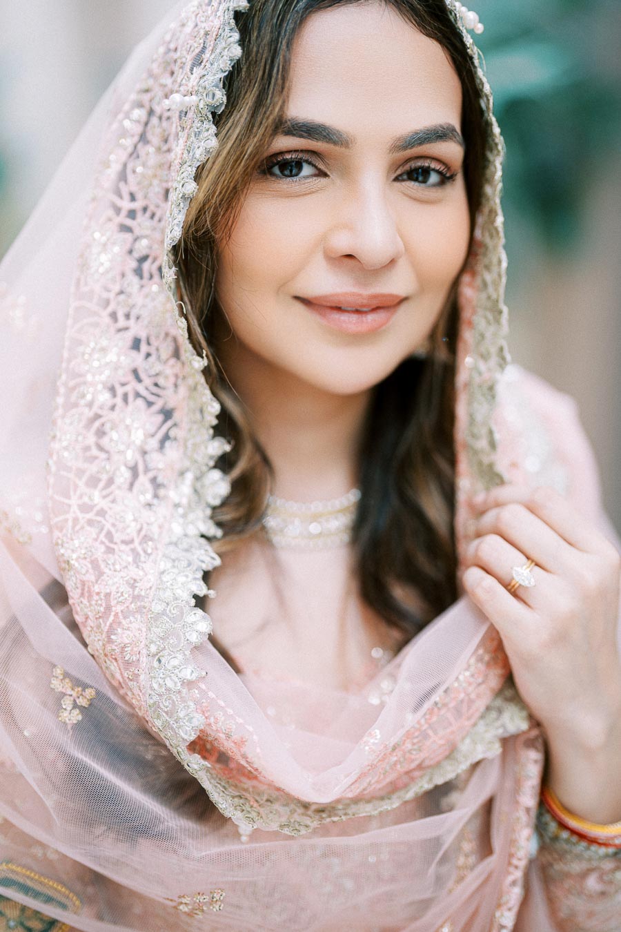 Woman in elegant pink embroidered traditional attire with delicate jewelry and a soft smile.