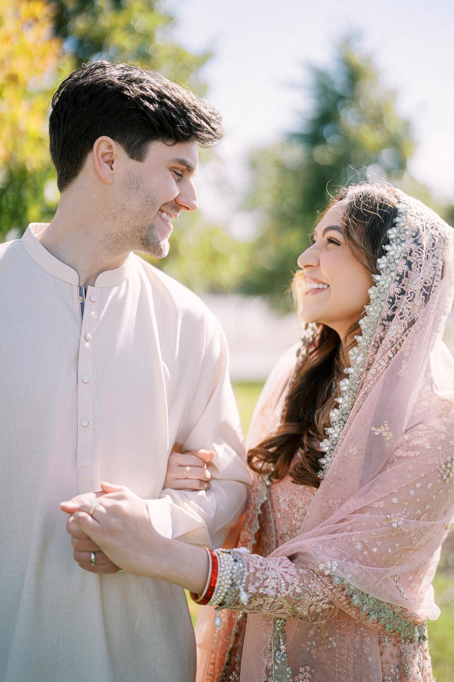 Smiling couple in traditional attire enjoying a sunny outdoor moment, with greenery in the background.