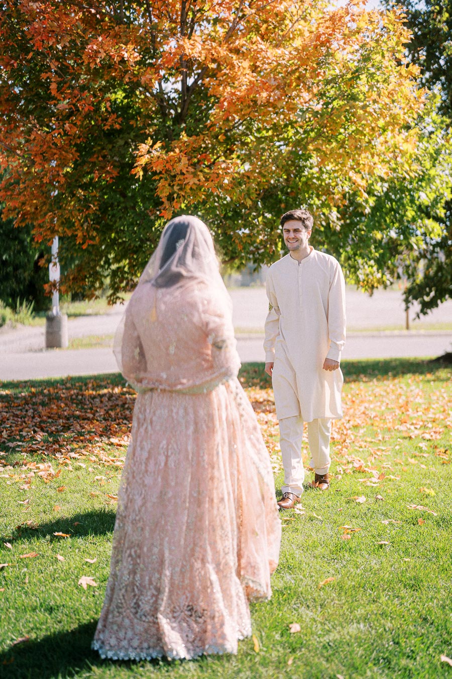 A couple in traditional attire celebrating an outdoor wedding during autumn, with vibrant fall foliage in the background and sunlight filtering through the trees.