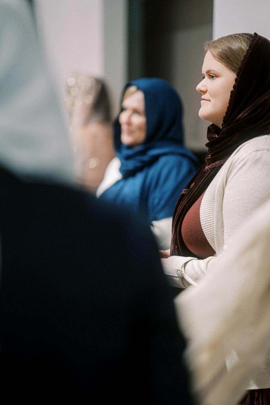 Women wearing scarves gathered in a room, focused on an event or conversation.