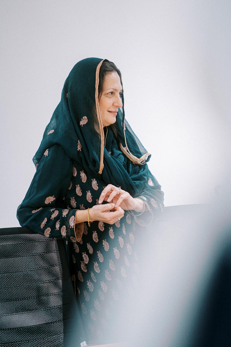 A woman wearing a traditional green patterned scarf and dress, standing indoors and smiling, with a focus on cultural attire in a professional setting.