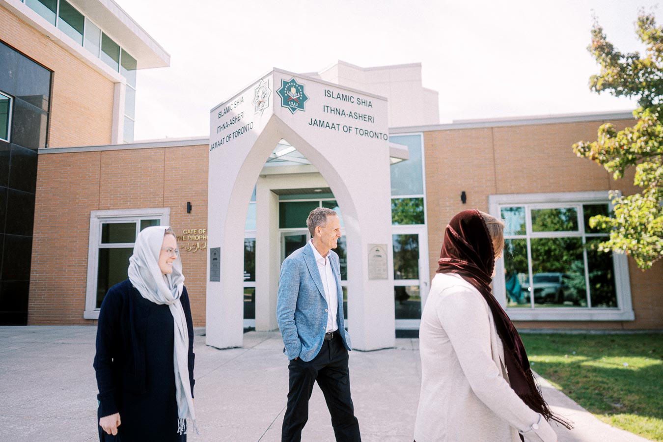 People walking outside the Islamic Shia Ithna-Asheri Jamaat of Toronto building under a clear sky.