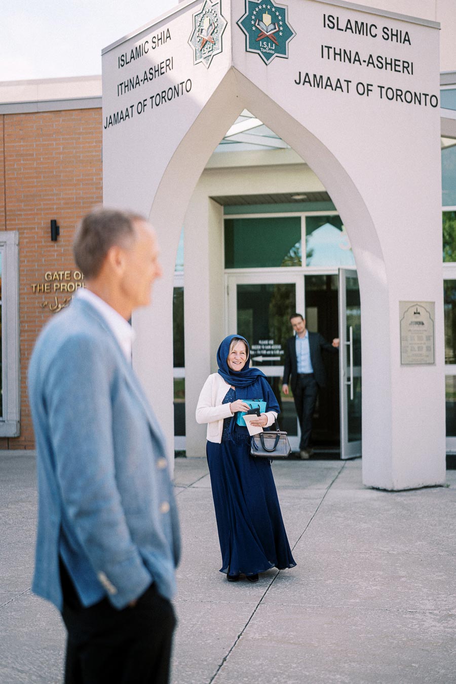 People gathered outside the Islamic Shia Ithna-Asheri Jamaat of Toronto mosque, featuring entrance signage.