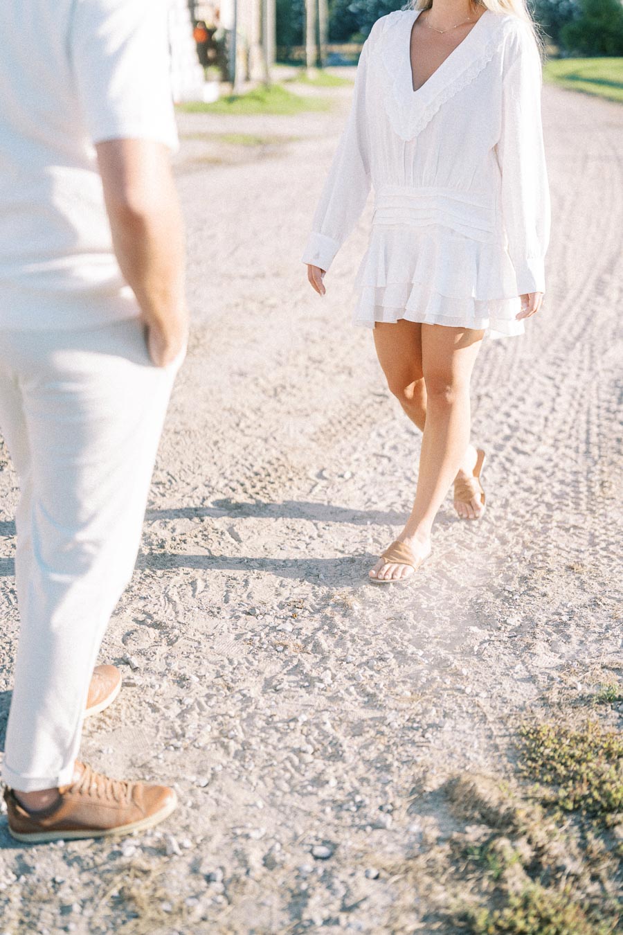 A man and woman in casual white attire walking on a sunny gravel path.