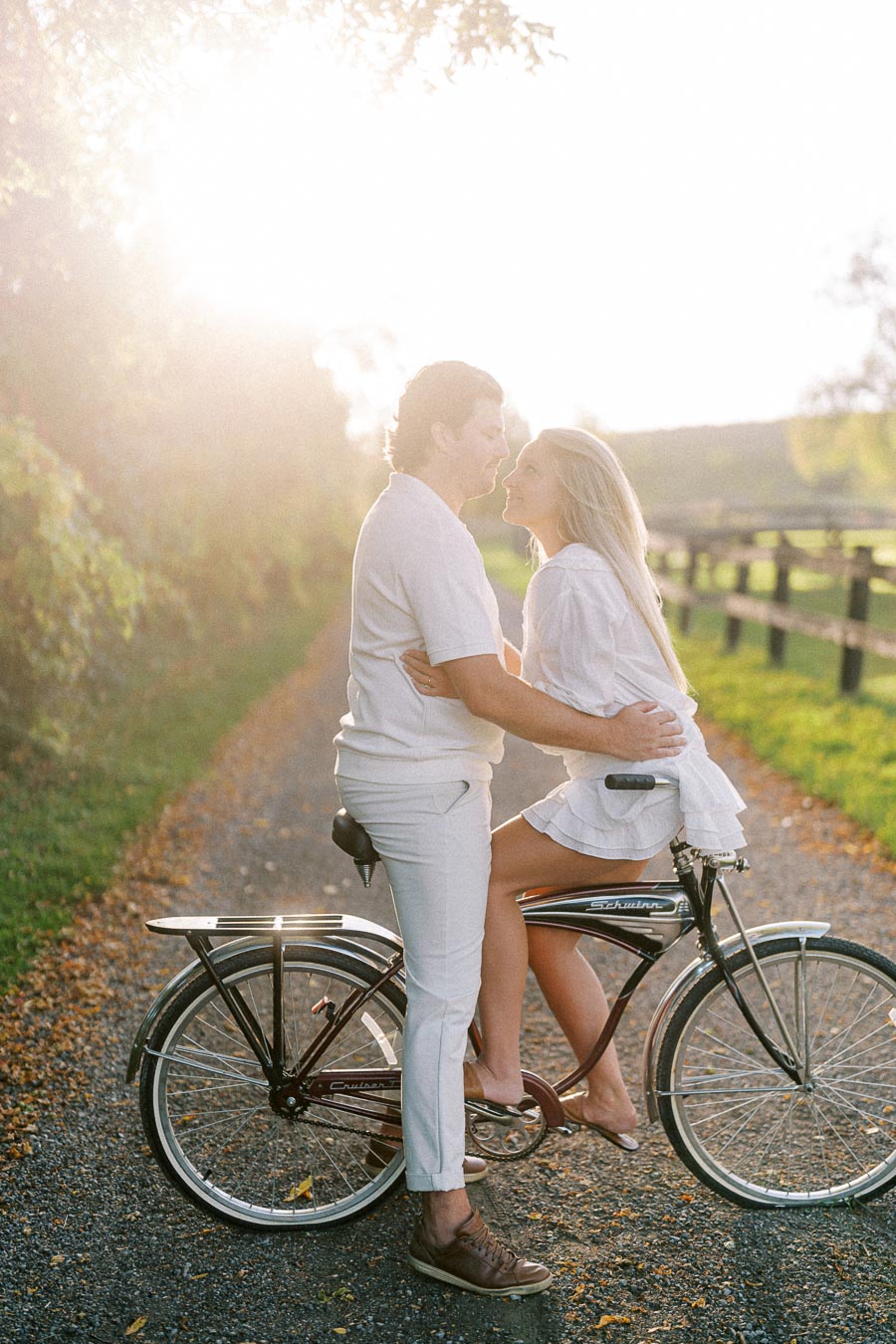 Romantic couple sharing a tender moment on a vintage bicycle during sunset on a scenic rural path.