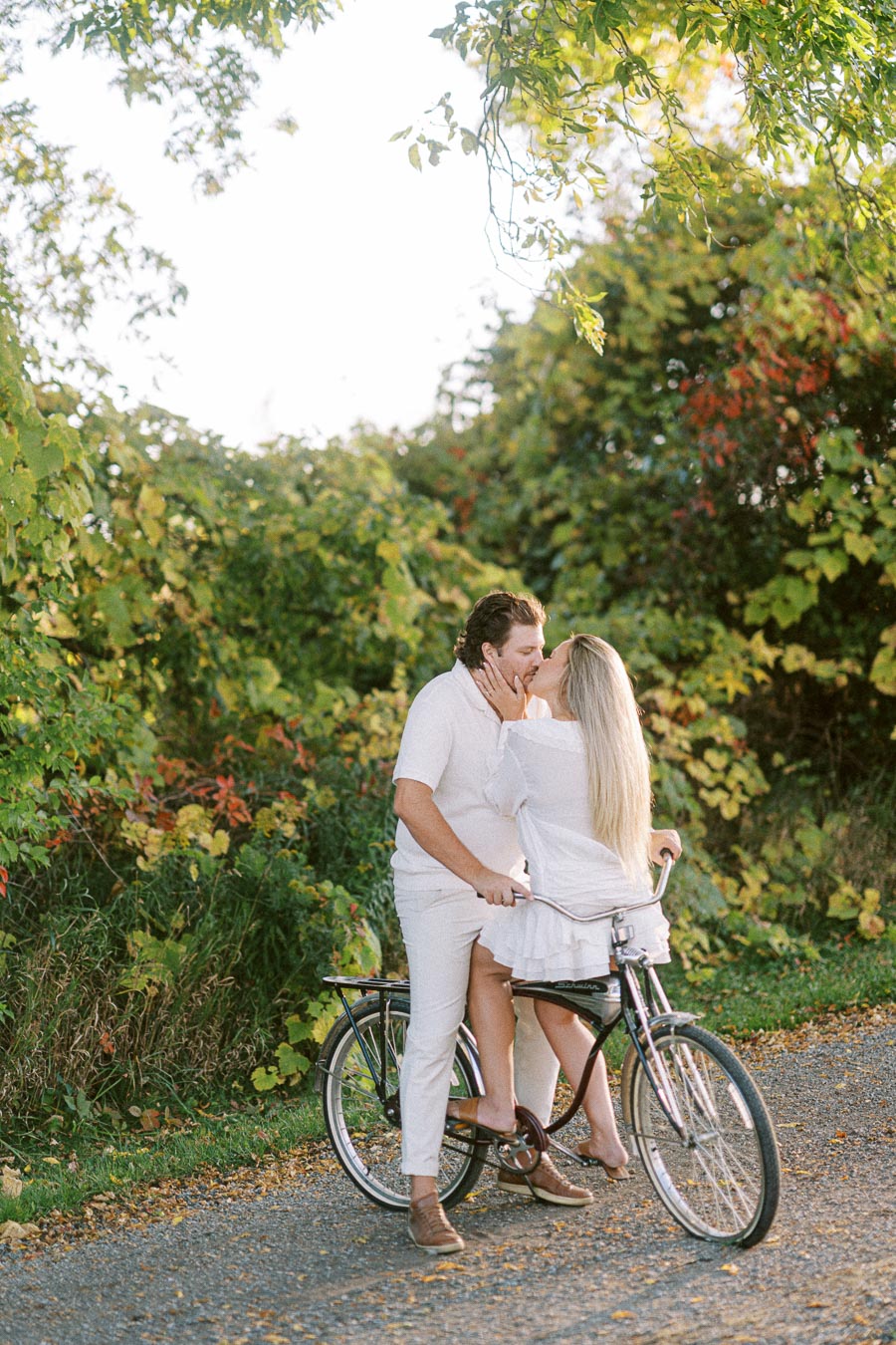 A couple sharing a romantic moment on a bicycle in a lush, green outdoor setting with abundant foliage.