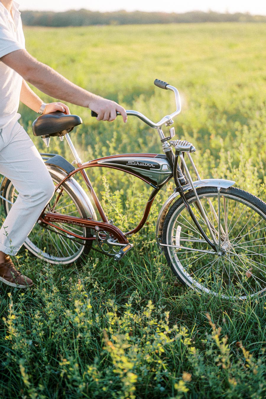 A person in white pants riding a vintage Schwinn bicycle across a sunlit green field, emphasizing leisurely outdoor activity and classic bike design.