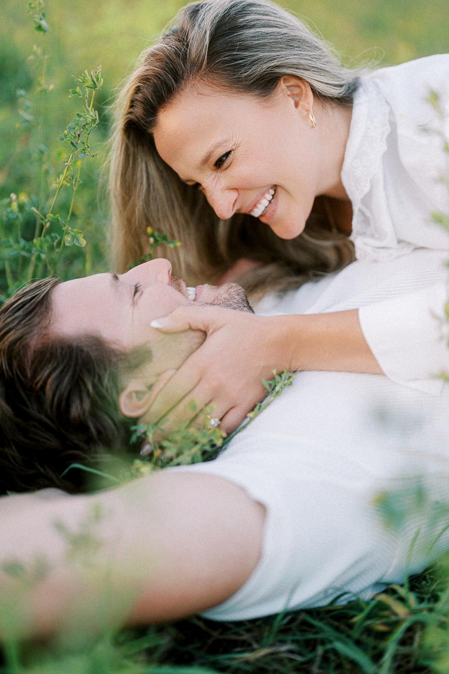 Happy couple lying in a grassy field, smiling at each other and holding hands, depicting love and joy in nature.