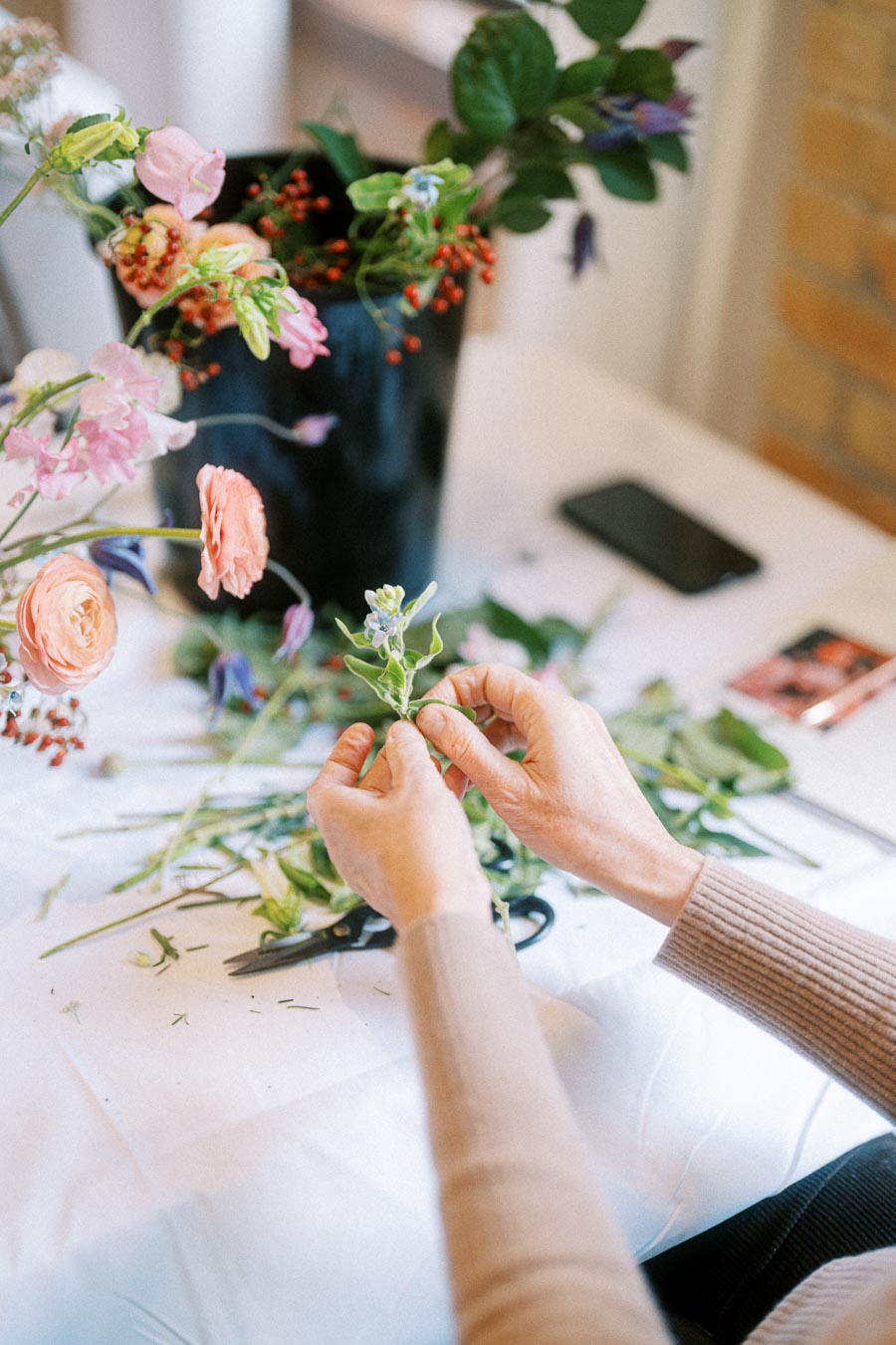 Florist arranging a colorful bouquet with fresh flowers on a table, surrounded by floral materials and tools.