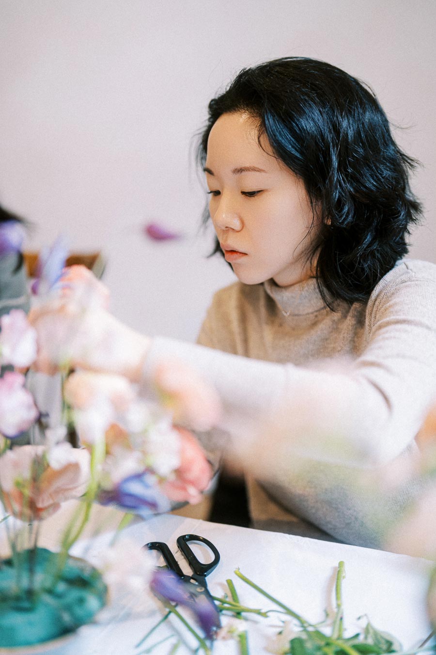 Florist arranging a colorful bouquet of flowers on a table, with scissors visible in the foreground.