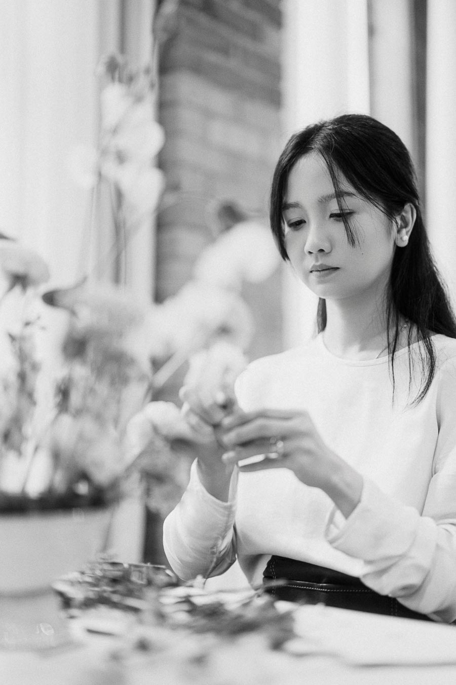 Black and white image of a woman focusing on creating floral arrangements indoors, wearing a light-colored top.