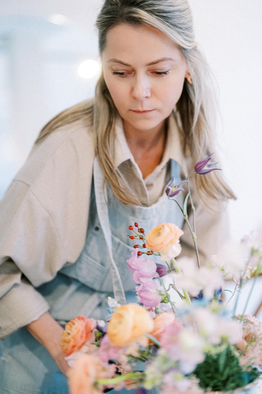 Florist arranging colorful bouquet with pink, orange, and purple flowers in a studio setting