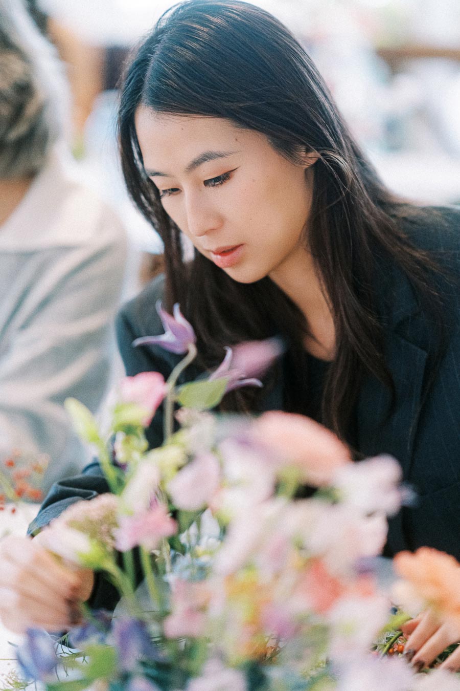 Young woman arranging an elegant floral arrangement, focusing intently on colorful flowers in a workshop setting.