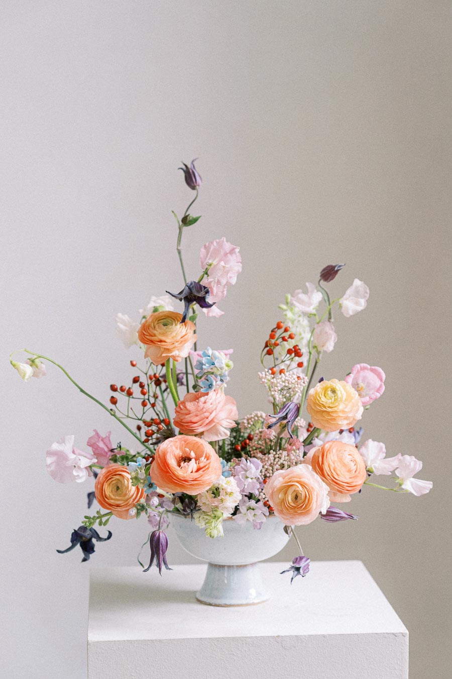 Elegant floral arrangement in a white vase featuring pastel-colored ranunculus, delicate sweet peas, and a variety of seasonal blooms for a spring-inspired centerpiece.