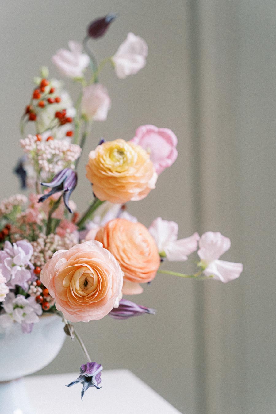 A beautiful floral arrangement featuring pastel-colored roses, delicate pink and white flowers, and vibrant red berries in a white vase.