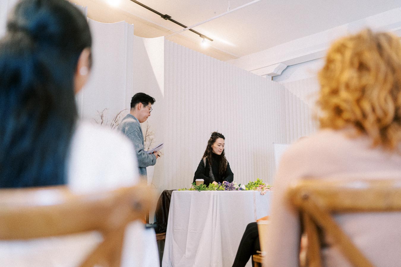 A group of people attending an indoor seminar with a focus on leadership and strategy development. The speaker is standing near a podium with notes, engaging with the audience in a modern conference room.