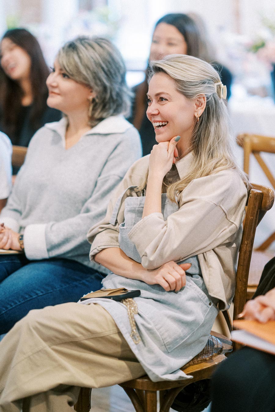 A group of people smiling and engaged during a meeting or workshop, seated with notebooks on their laps, capturing a positive and interactive learning environment.