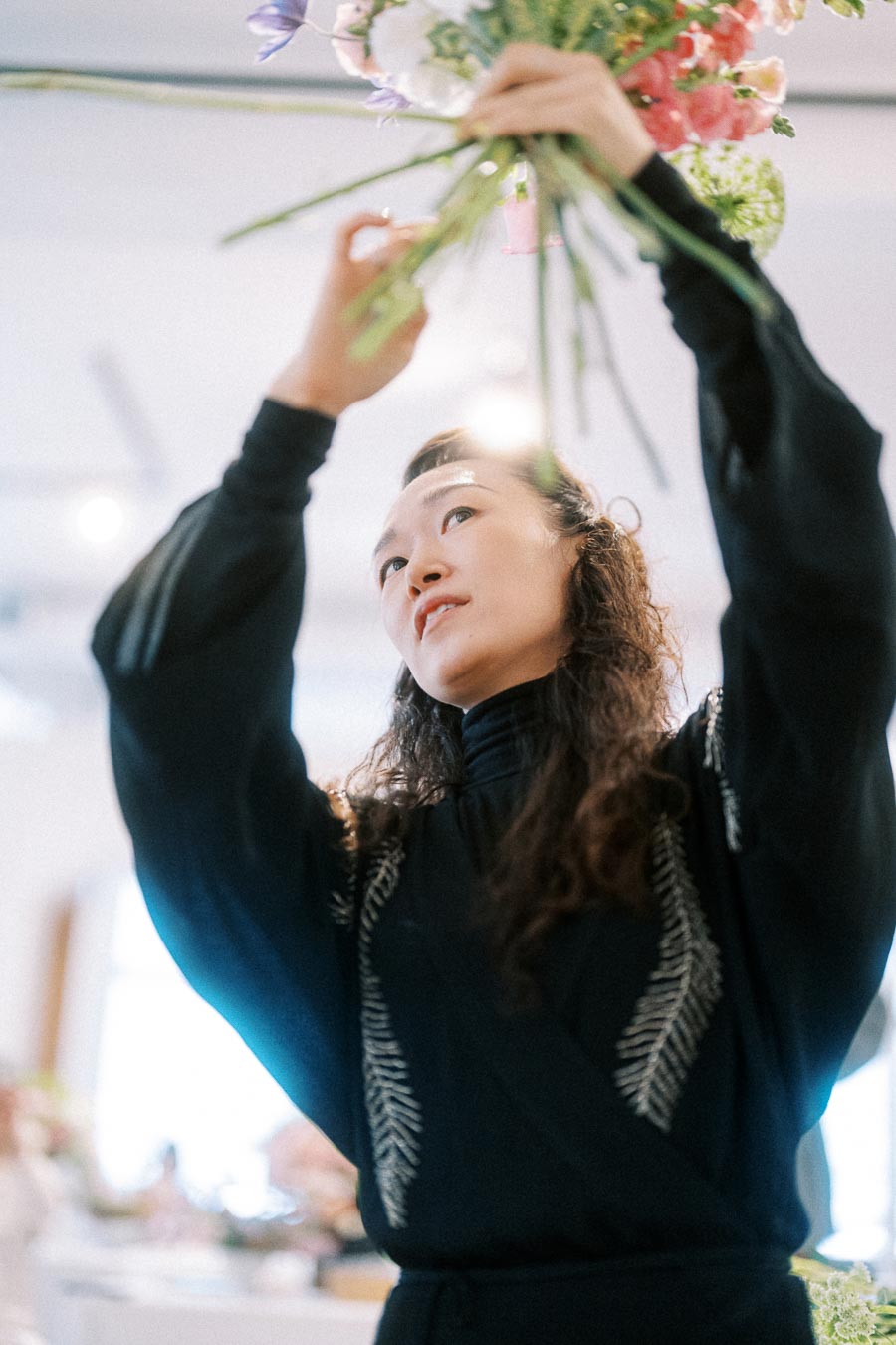 A person arranging a colorful bouquet of flowers, focused and creative in a bright room.