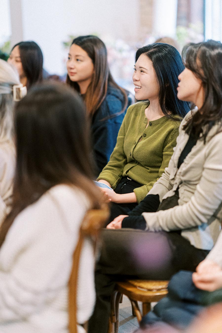 Group of attentive women sitting and engaging in a seminar session, wearing casual attire in a brightly lit room.